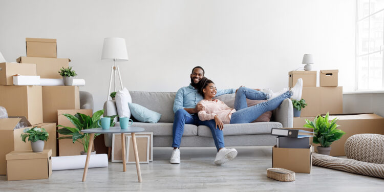young african american husband and wife relaxing on couch in living room with cardboard boxes